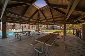 A wooden deck with picnic tables and a pool in the background.
